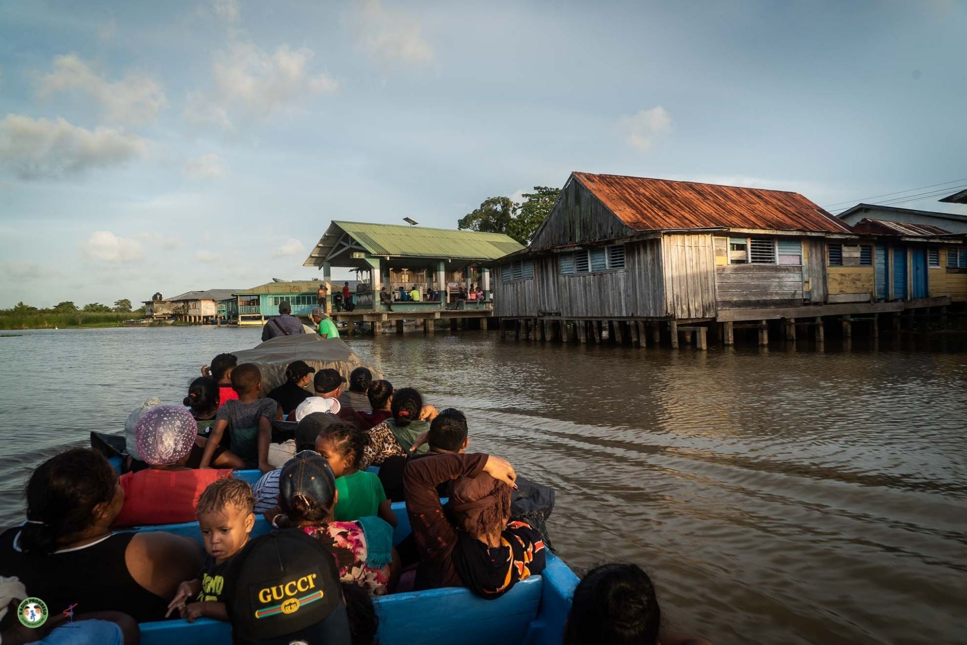 Grupo de personas viajando en lancha por el río, entre viviendas palafíticas